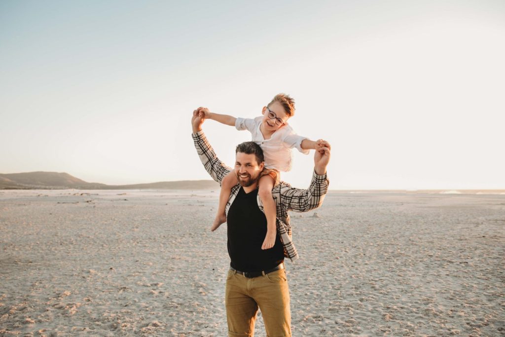 Father lifting child in the air during playful family photo shoot on Cape Town’s Noordhoek Beach