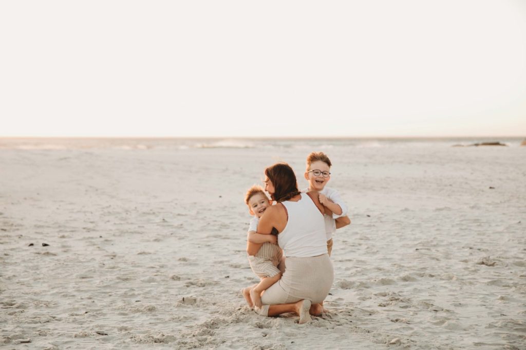mom huggin gher kids on the noordhoek beach during a family photo shoot