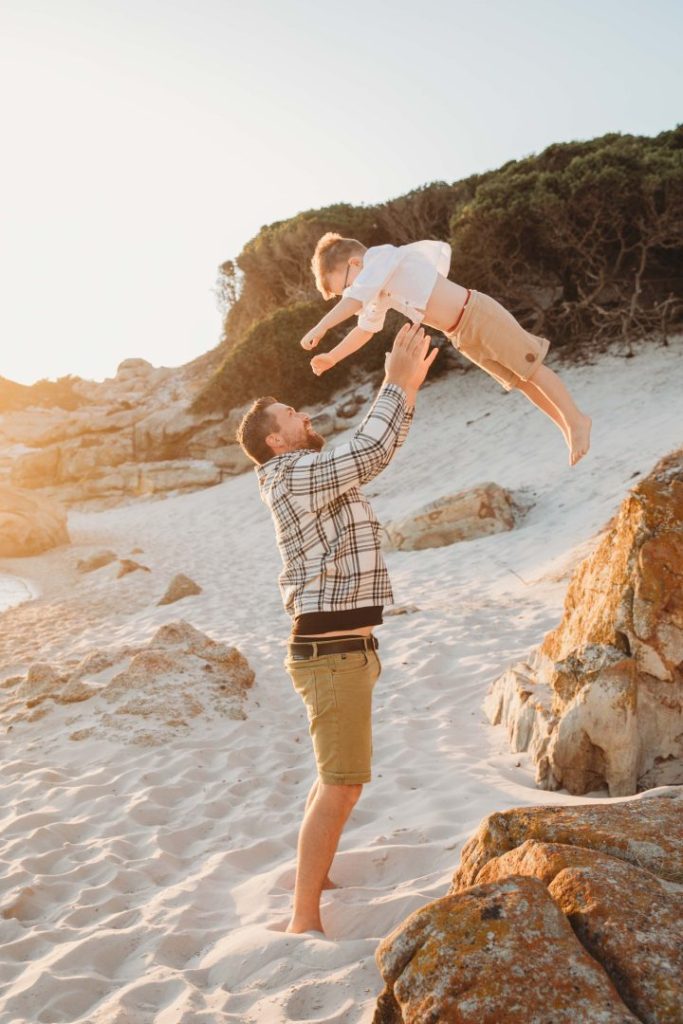 Father lifting child in the air during playful family photo shoot on Cape Town’s Noordhoek Beach