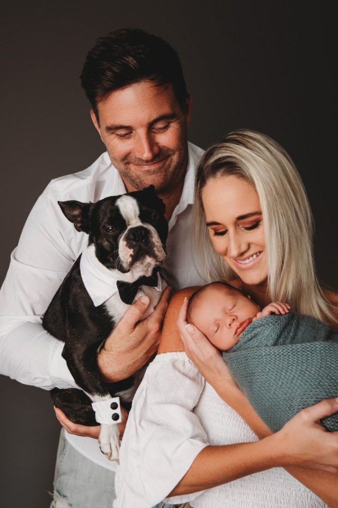 Studio portrait of a newborn baby held by parents with their dog