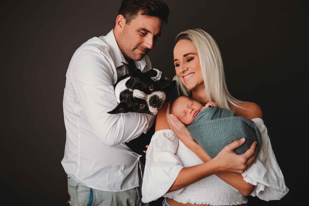 Studio portrait of a newborn baby held by parents with their dog