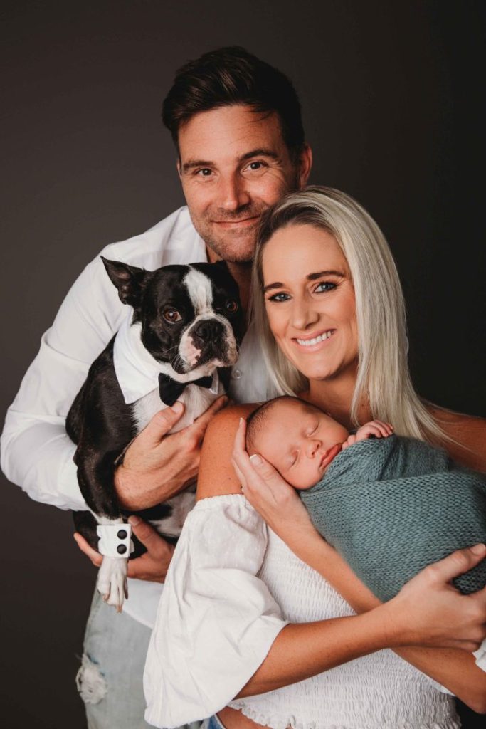 Studio portrait of a newborn baby held by parents with their dog