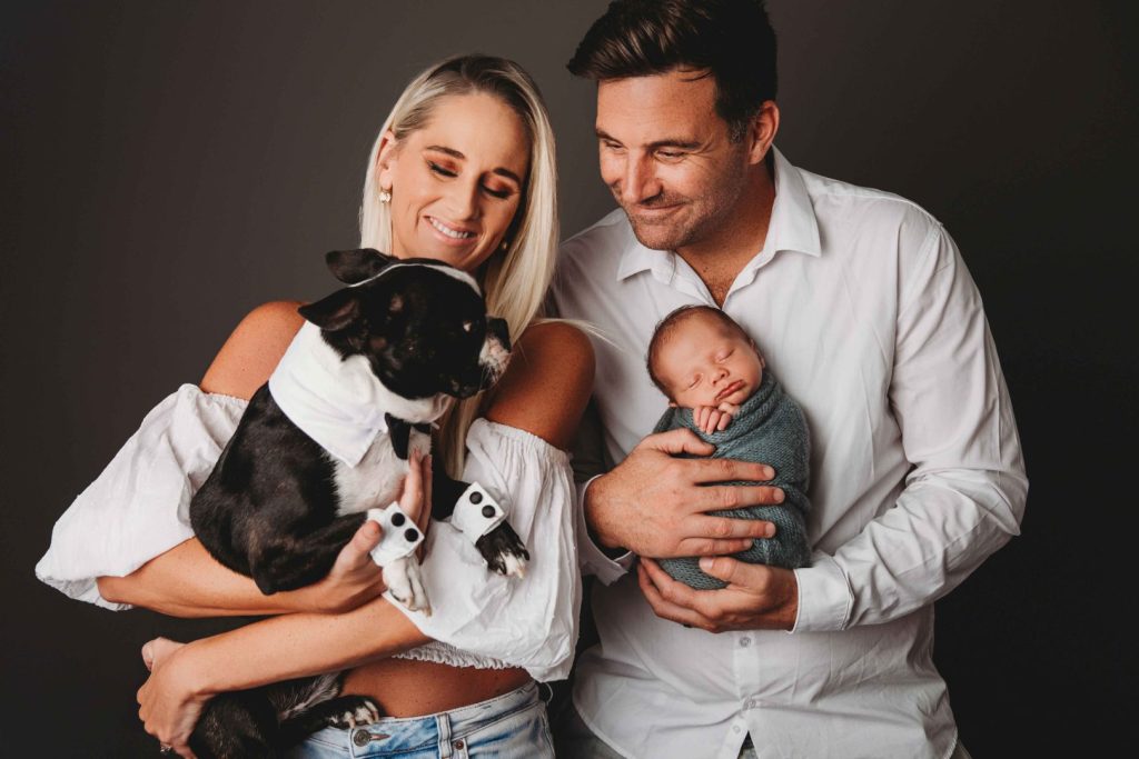 Studio portrait of a newborn baby held by parents with their dog
