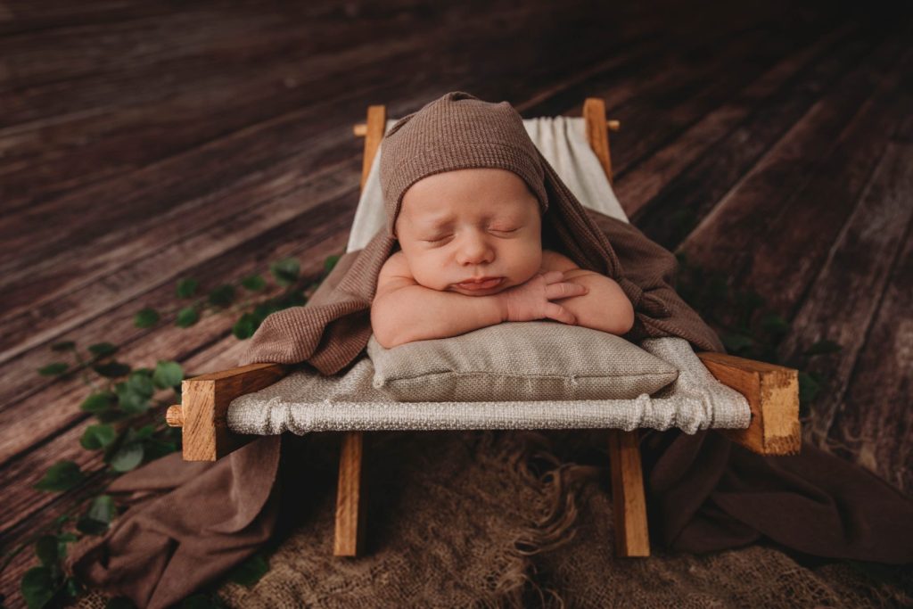 Studio portrait of a posed newborn in a woven basket, wearing a knitted bonnet