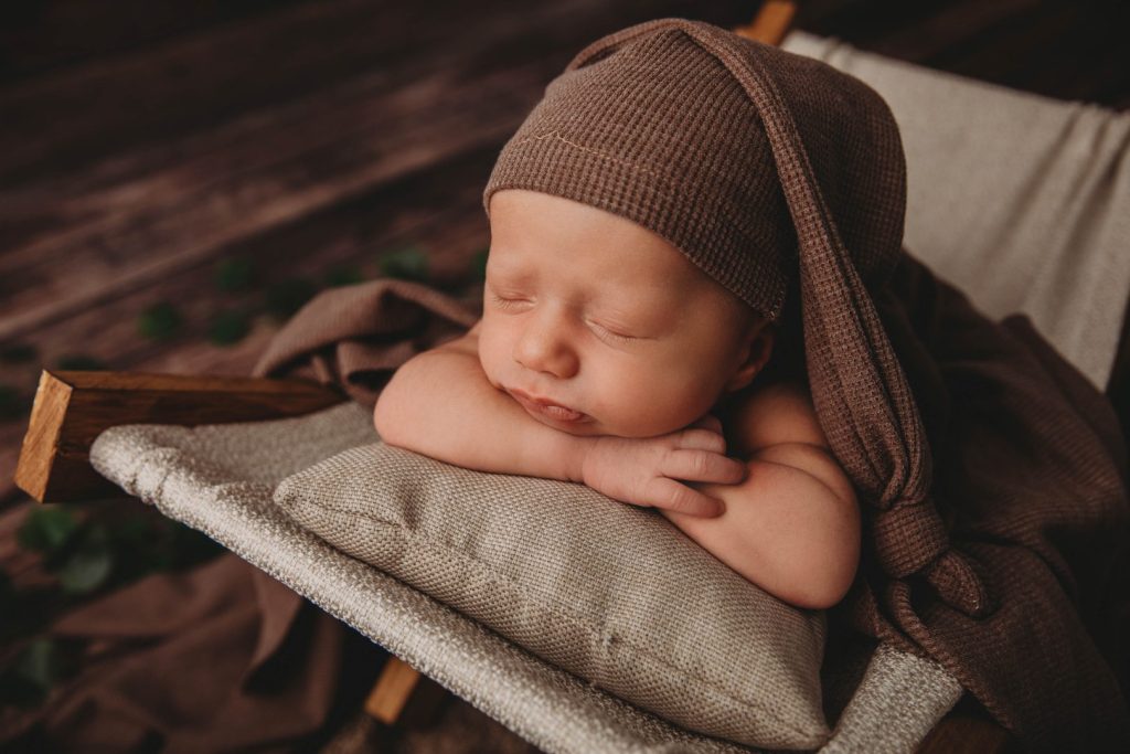 Studio portrait of a posed newborn in a woven basket, wearing a knitted bonnet,