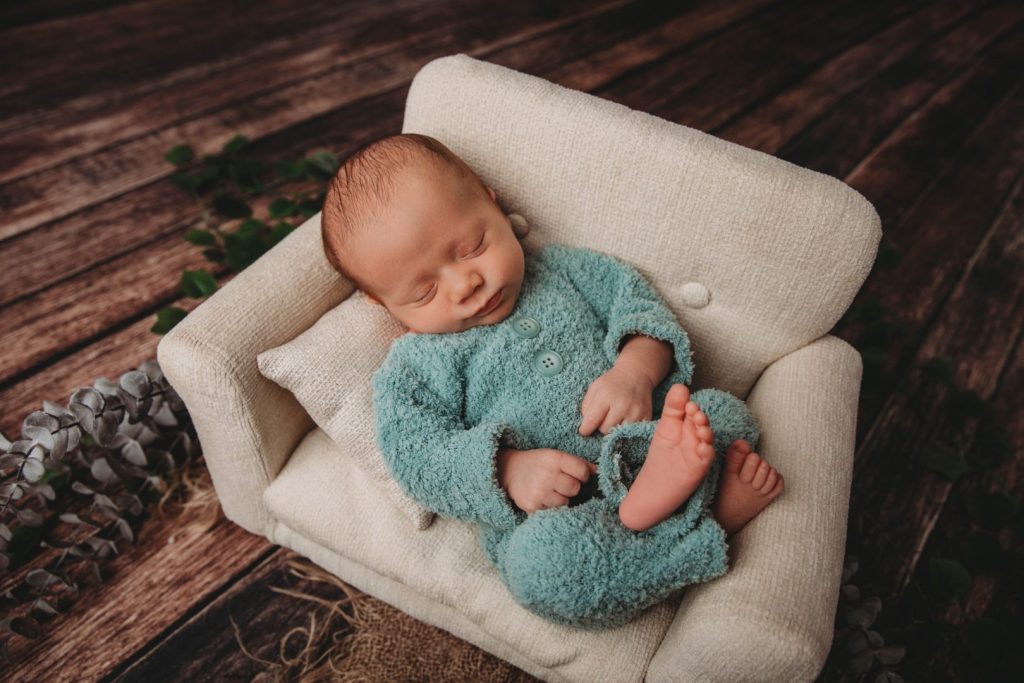 Studio portrait of a posed newborn in a small couch, wearing a knitted outfit,