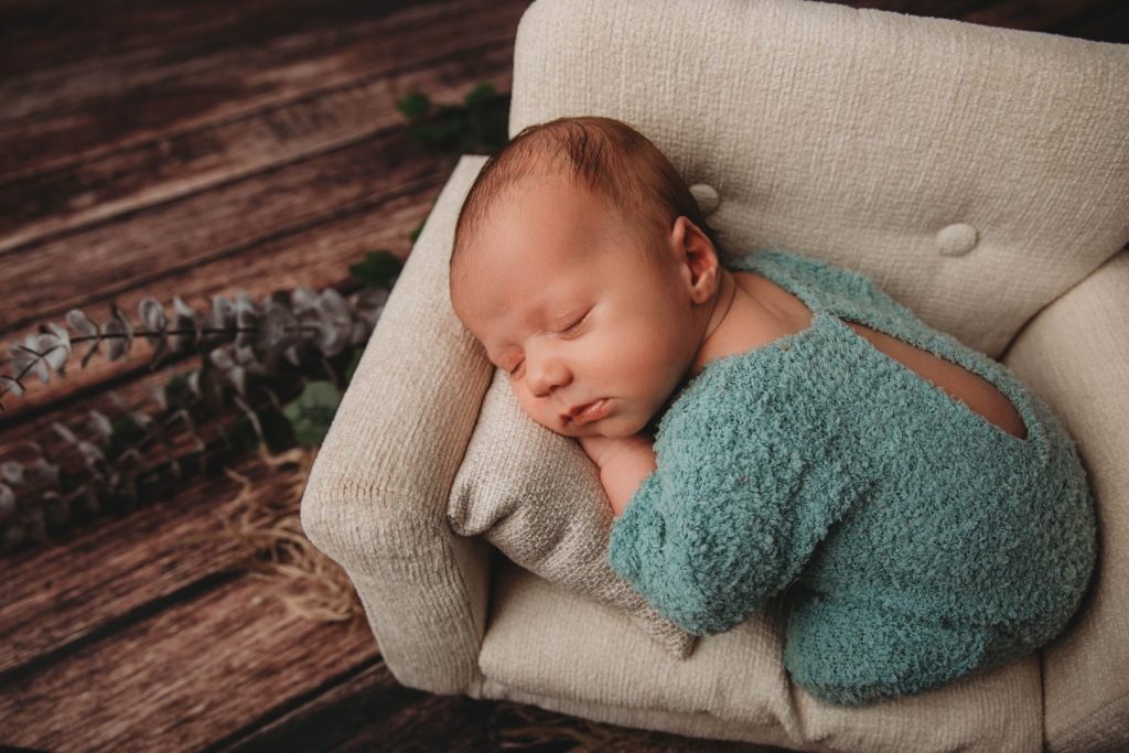 Studio portrait of a posed newborn in a small couch, wearing a knitted outfit,
