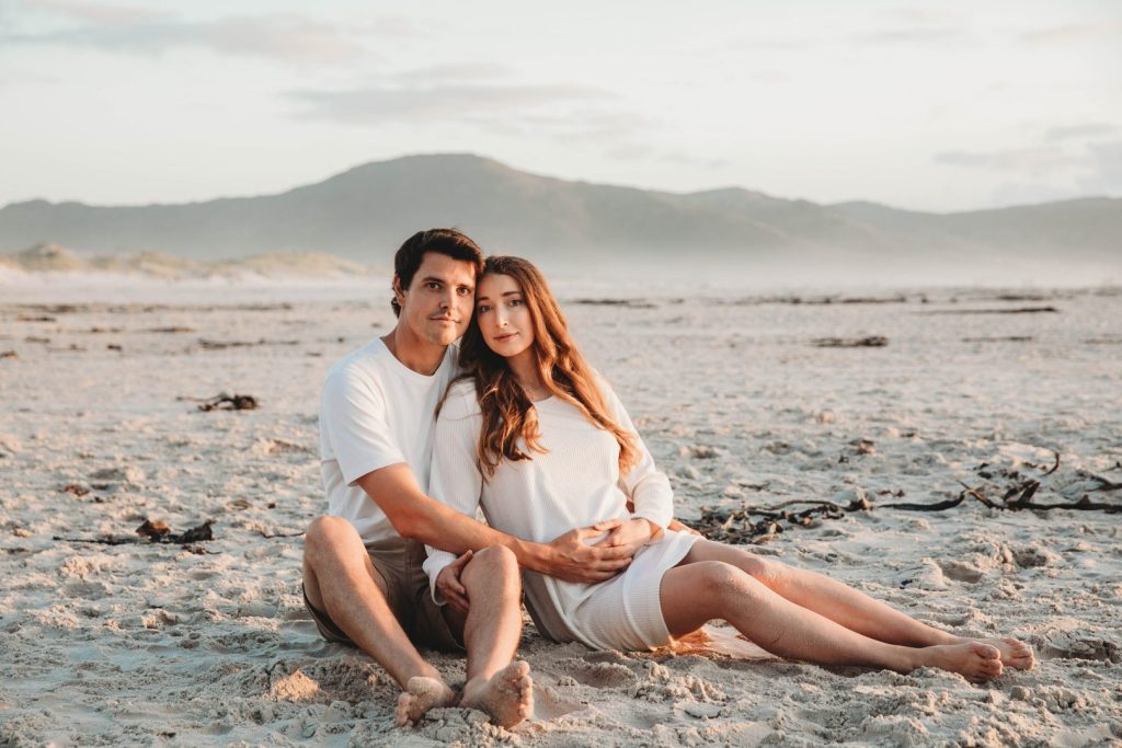 Pregnant woman walking barefoot on Noordhoek Beach at sunset