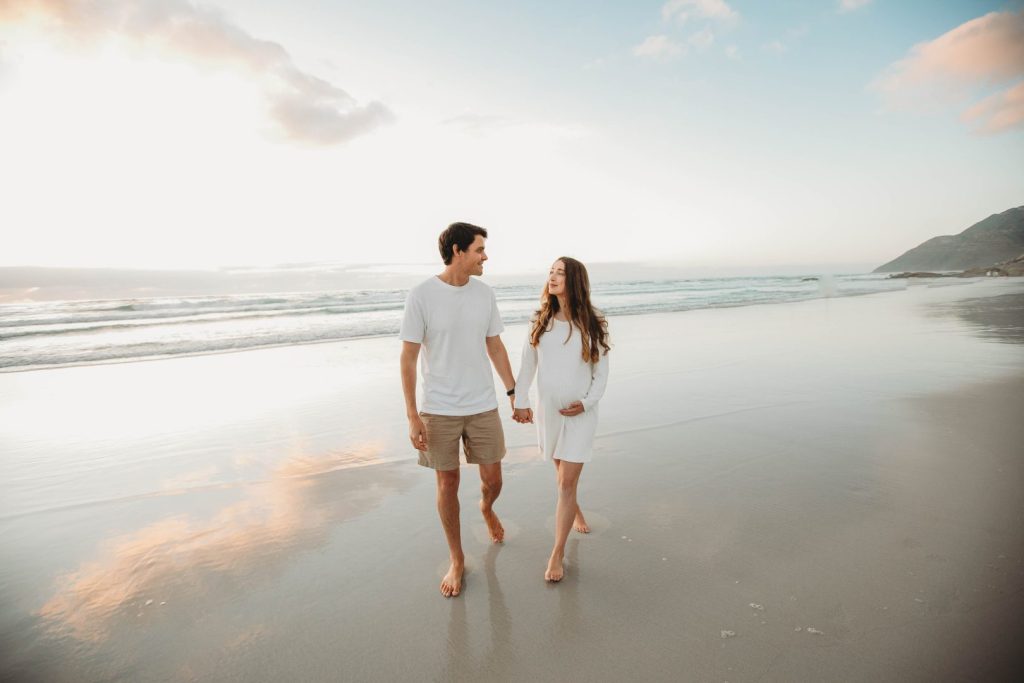 Expectant mother posing on Noordhoek dunes with ocean in the background