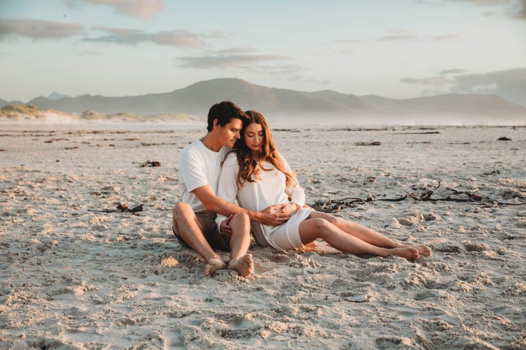 Pregnant woman walking barefoot on Noordhoek Beach at sunset