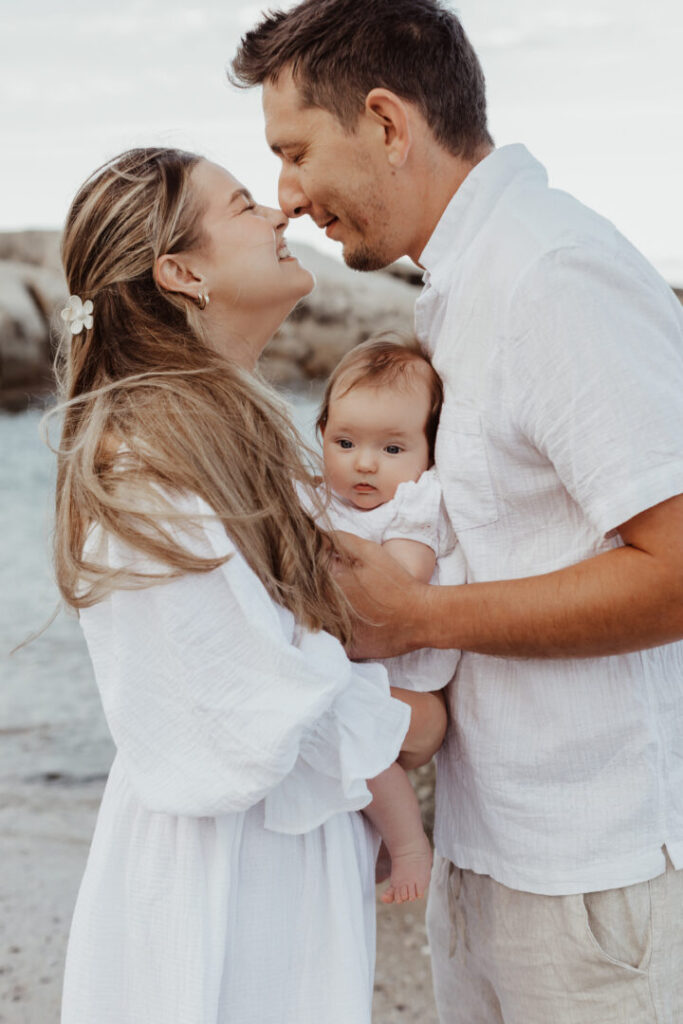 Family of three with baby wearing white outfits on Bakoven Beach in Cape Town