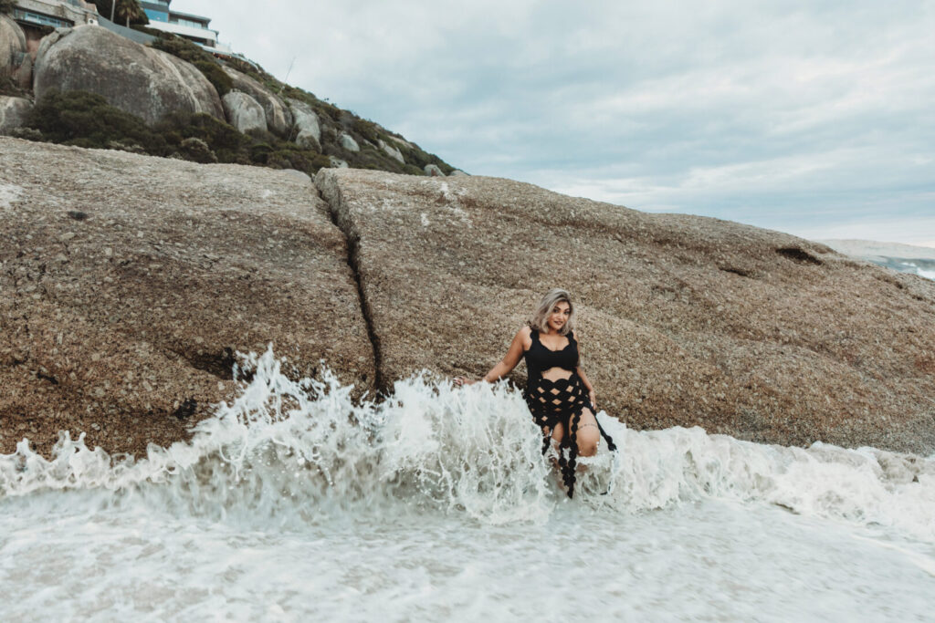 Pregnant woman wearing a black dress posing on Llandudno Beach in Cape Town during a maternity photo session