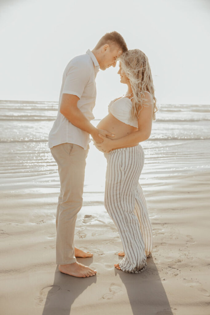 mom and dad to be embracing at sunset during pregnancy