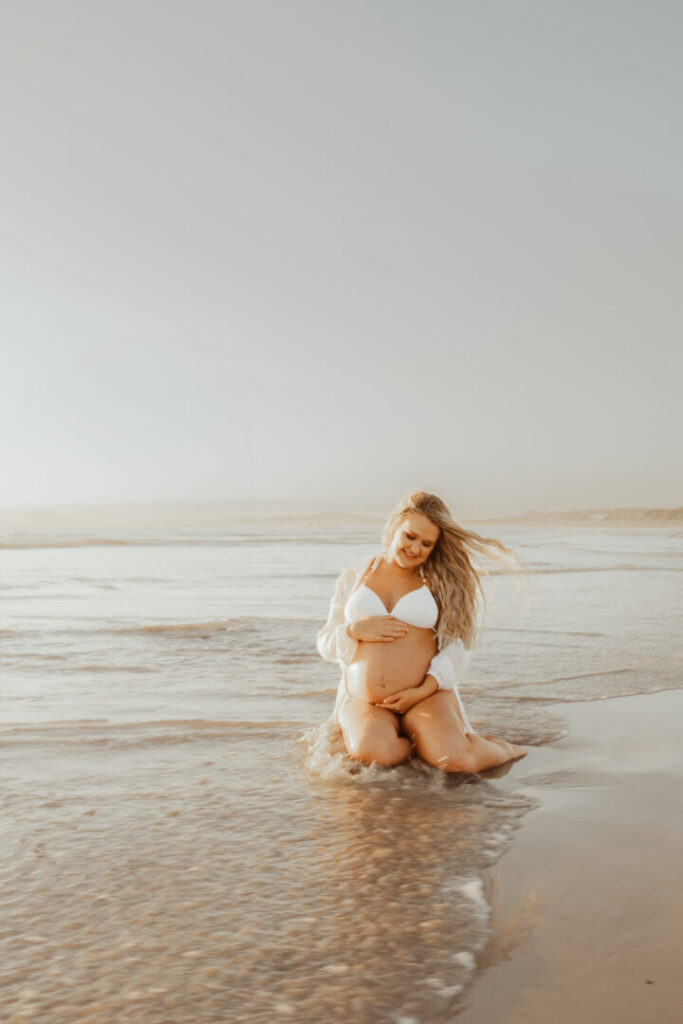 pregnant mom in the ocean wearing white at sunset