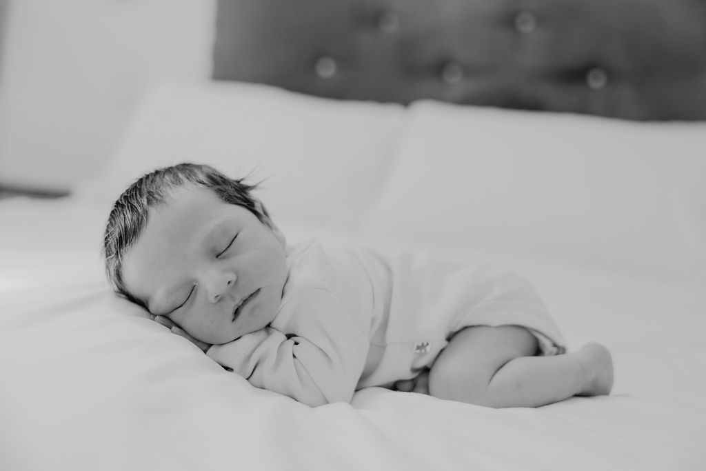 black and white photo of baby on king size bed sleeping 