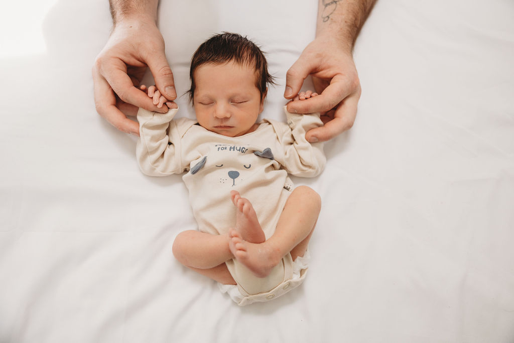 Newborn baby holding dads hands at photo shoot 